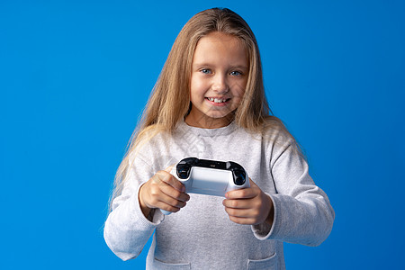 年轻可爱的女孩玩电脑游戏 用蓝背景的摇杆打滚棍玩家控制器孩子们女士活动安慰微笑闲暇电子游戏爱好图片