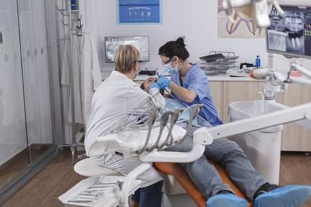 配有医疗面罩的矫形小组在病人牙齿上工作临床口服药品程序治疗咨询钻头健康卫生员感染图片
