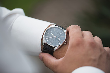 特写的商务人士看着他手上的手表在户外 自由空间 穿白衬衫的男人用豪华手表检查时间 手表在手 新郎婚礼准备图片