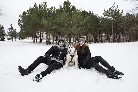 美丽的家庭 一个男人和一个女孩与狗一起在冬季森林玩狗西伯利亚哈斯基帽子乐趣松树女孩石头喜悦宠物动物笑声幸福图片