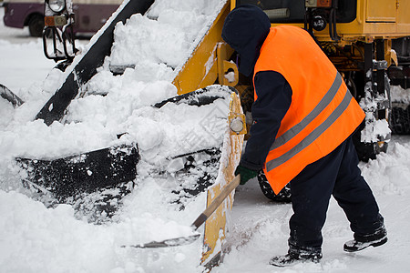 爪式装载机车辆清除道路上的积雪 市政服务的员工帮助将雪铲入扫雪机图片