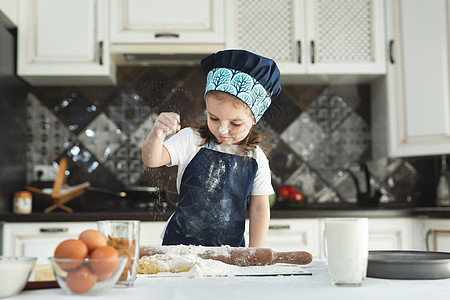 一个穿围裙的小女孩 和厨师帽子 把面粉洒在厨房里图片