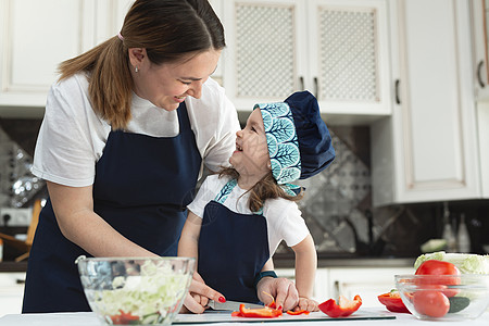 有爱心的母亲教她的小女儿如何在厨房里准备沙拉 一位年轻的母亲和一个迷人的甜美女婴相视而笑图片