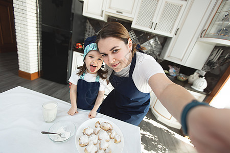 妈妈和她的女儿在家里的现代厨房里烤饼干并自拍图片