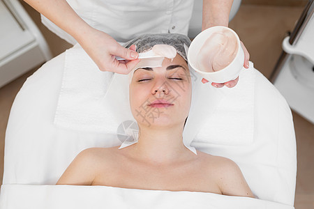 面部去角质面膜 水疗美容 护肤 美容师在 spa 沙龙接受面部护理的女人 女人制作藻酸盐面膜 戴着米色粘土面具的女孩化妆品身体奶图片