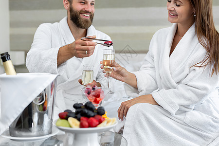 在床上的旅馆里 男人把浆果放在一杯起泡酒里给他的女人图片