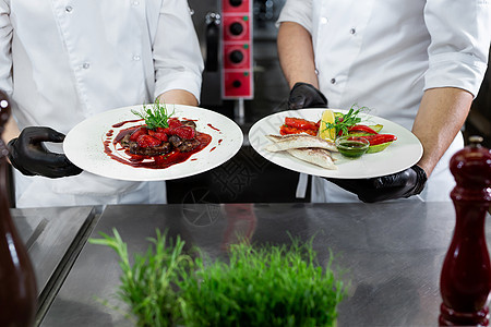 一个专业厨房的两名厨师手里拿着现成的盘子男人餐厅工作职业帽子用餐服务食物餐饮蔬菜图片