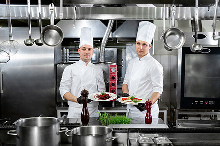 一个专业厨房的两名厨师手里拿着现成的盘子手套餐厅男性服务帽子成人男人食物蔬菜工作图片