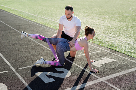 教练在体育场跟一个年轻女孩一起玩运动 用弹性乐队练习腿部运动图片