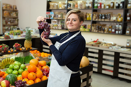 女售货员帮助顾客在杂货店购买水果和蔬菜 将果子握在她的手中 并展示葡萄图片
