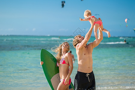 年轻和美丽的父母在海滩上玩弄他的女儿 笑声旅行冒险海滩乐趣泳装假期父亲家庭冲浪者天空图片