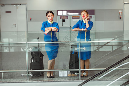 机场终端站着两名携带旅行袋的女空姐空气女士行李航空宪章手提箱飞机工作旅行职业图片