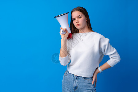 女孩在蓝色工作室用扩音器做广告讲话女士喇叭青少年休闲装女性嗓音演讲扬声器注意力图片