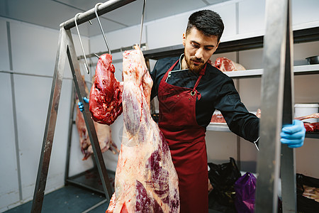 男性屠夫站在肉店的肉架上猪肉产品施工男人微笑鱼片红色围裙职业店铺图片