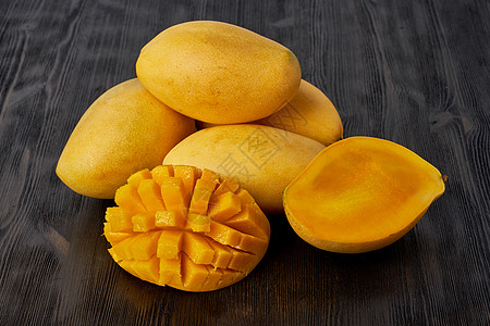 四个完整的芒果水果放在木桌上 切成薄片 大多汁明亮成熟的黄色水果图片