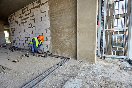 身着防护服和安全帽的工人或建筑商正在使用现代工具在正在建设的建筑物中安装塑料管图片