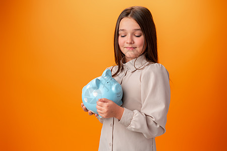 穿橙色背景的小猪银行的少女女士信用财富学校青少年货币孩子投资硬币现金图片