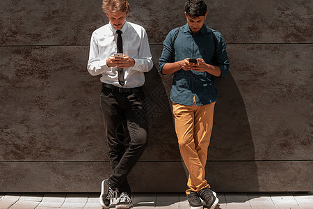 休闲的多民族创业商务人士 其中一位是印度人 在下班休息时在外面的灰墙前使用智能手机衬衫职业工作团体商业套装公司电脑技术学生图片