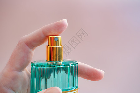 女性手中的美丽现代香水瓶 以绿色透明玻璃和粉红底金盖为绿色颜色的极小化风格图片
