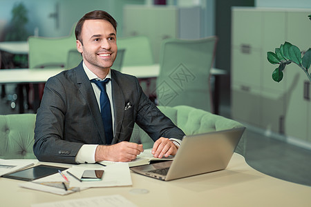 穿着西装的英俊男子在笔记本电脑上工作 工作正在进行中 欢呼微笑的自由职业者坐在明亮的联合办公空间里 在调度程序中做笔记男性经理互图片