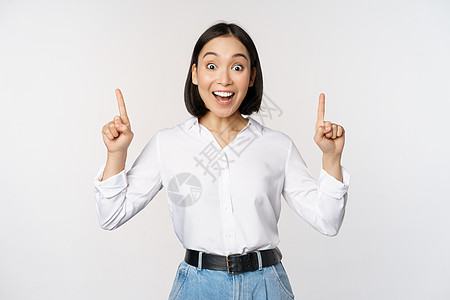 热情的女商务人士 亚洲女模特指着手指微笑 发布公告 在顶部展示标志横幅 白色背景企业家女性公司人士女士快乐女孩成人广告员工图片