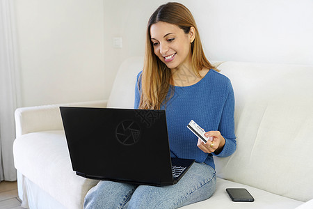 巴西美女坐在家里的沙发上 用信用卡和笔记本电脑在网上购物图片