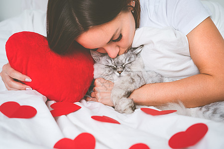 女人躺在床上 用红心吻她可爱的猫咪 爱宠物 情人节的概念图片