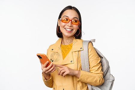 时尚的年轻女性女游客 带背背包和智能手机旅行者在镜头下微笑 以白色背景装扮技术企业家互联网办公室女士黑发商业广告情感大学图片