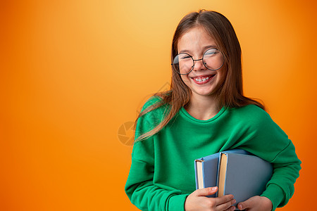 有着橙色背景书籍的聪明少女女孩的肖像知识笔记本瞳孔头发孩子家庭作业教育班级孩子们文学图片