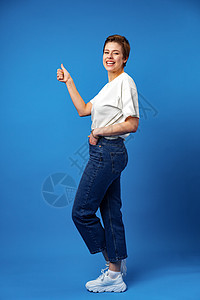 年轻快乐的少女 短发短发 在蓝背景上举起拇指图片