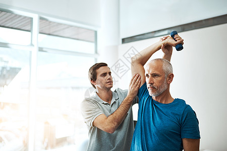 这些练习对您的康复非常重要 拍摄一位年轻的男性物理治疗师白天在他的办公室帮助客户进行伸展运动图片