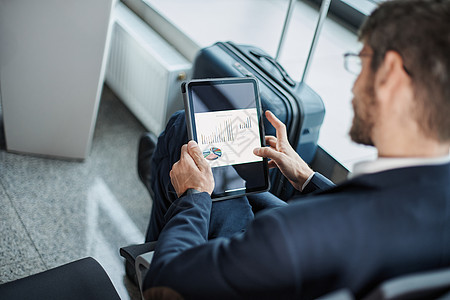 商务人士在商务旅行时使用数字平板电脑药片技术人士男性座位图表手提箱屏幕上网愿望图片