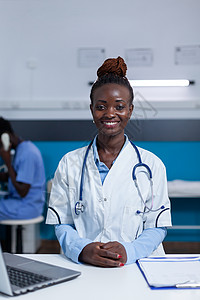 身着白大衣和听诊器的非洲美洲临床专家的肖像坐在桌子上图片