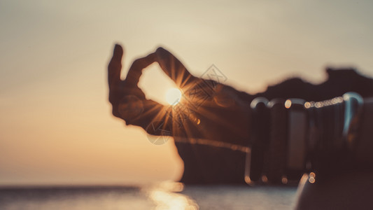 横幅 在模糊的特写镜头中 一个戴着手镯的年轻女子的手 在日落的海滩上练习瑜伽 保持手指连接 阳光透过它们 健康的生活方式 和谐的图片
