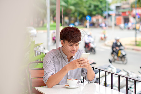年轻微笑的男人在户外咖啡馆看电话或阅读信息教育企业家手机网站细胞工作商务电话人士学生图片