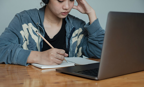 亚洲年轻女性写作列表的裁剪照片在记事本中做笔记在室内笔记本电脑上工作或学习-教育课程或培训 研讨会 在线教育概念图片