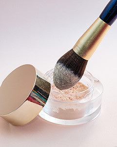 金色化妆刷被浸在玻璃罐里 粉红色背景的粉末图片