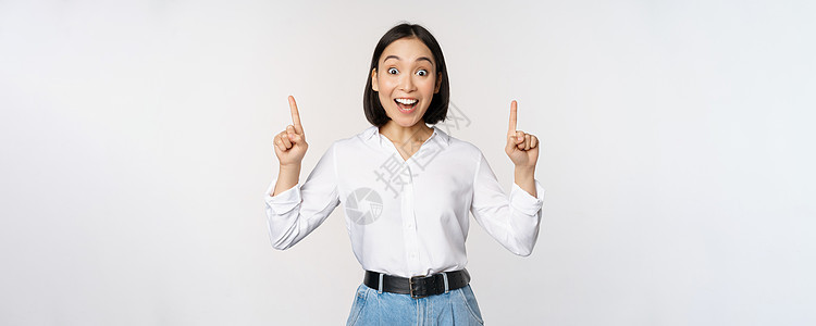 热情的女商务人士 亚洲女模特指着手指微笑 发布公告 在顶部展示标志横幅 白色背景管理人员公司售货员女士手臂女孩企业家工作室老板商图片