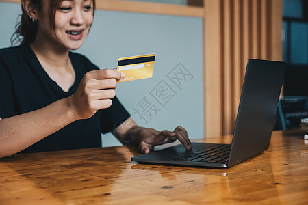 亚洲女孩持有银行信用卡并在笔记本电脑上打字 使用电脑在线购物 购买商品或在线订购 输入银行账户和在线银行报价中的详细信息的特写卡图片