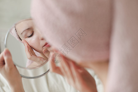 头戴毛巾的年轻女子看着镜子 在脸皮上涂奶油化妆品黑发眼睛面具治疗女孩身体粉刺清洁浴室图片