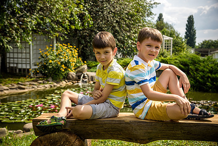 两个兄弟男孩坐在和平湖附近的公园的长凳上 有水 孩子们在炎热的夏日放松自然太阳闲暇青少年悲伤男生长椅孩子背包午休晴天图片