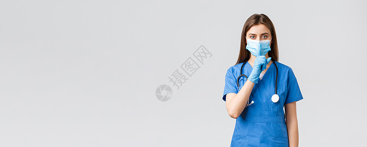 Covid19 预防病毒 健康 医护人员和检疫概念 压低声音 身着蓝色磨砂服 医用口罩和手套 嘘声 手指压在嘴唇上的严肃女护士胡图片