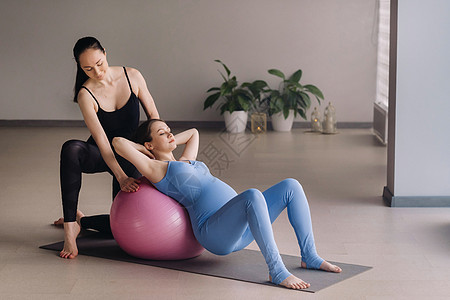 带球的健身班期间有教练训练员的孕妇瑜伽女孩孩子肌肉平衡腹部婴儿男人帮助女士图片