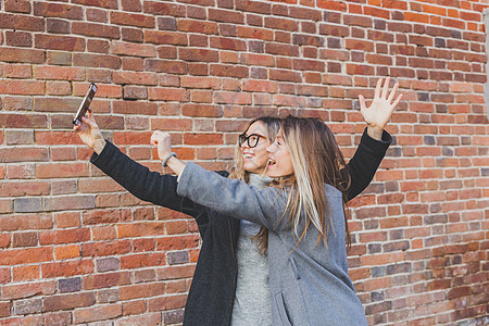 两位时髦女友在城市背景的社交网络上拍摄自相照友谊概念 掌声幸福女性摄影电话自拍街道乐趣快乐青少年照片图片