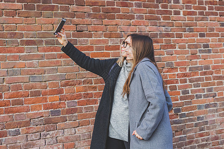 两位时髦女友在城市背景的社交网络上拍摄自相照友谊概念 掌声朋友们快乐自拍学生摄影潮人女孩派对电话乐趣图片