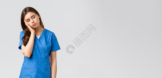医护人员 预防病毒和医学概念 疲倦昏昏欲睡的女医生 身穿蓝色磨砂服的年轻护士 靠在手掌上 闭上眼睛 在抗击冠状病毒的诊所夜班中筋图片