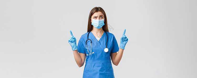 Covid19 预防病毒 健康 医护人员和检疫概念 身穿蓝色磨砂服 听诊器和医用口罩 持怀疑态度和多疑的女护士 指指点点擦洗管子图片