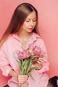 一个甜美迷人的女人 在粉红色的背景上穿着粉红色的裙子 微笑 幸福和幸运快乐青年展示冒充女士花束花朵情感工作室喜悦图片