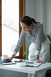 光彩照人的女性企业家 愉快的亚洲女商务人士站着并使用笔记本电脑图片