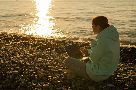 白种女人用笔记本电脑通过视频电话 在小石头海滩上交流互联网海滩网络技术教育蓝色海浪帽衫讲话旅行图片